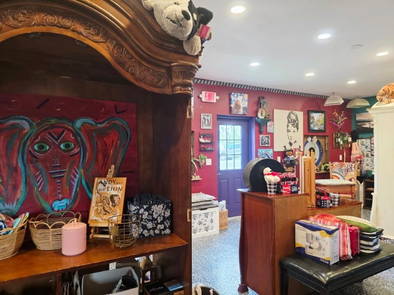 Carved wooden shelving displaying artwork and baskets beside the shop’s red-walled interior