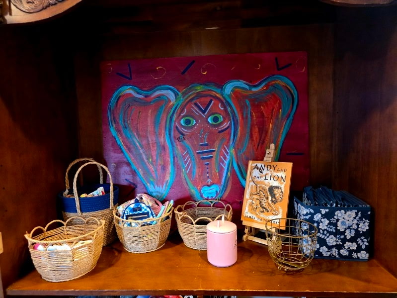 A colorful elephant painting with baskets and small objects on a wooden shelf